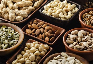 Assorted nuts and seeds in clay bowls on wooden kitchen table