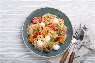 Delicious spaghetti with mozzarella, colourful cherry tomatoes, fresh basil on ceramic plate on