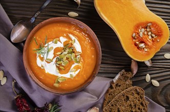 Flat lay view at homemade rustic pumpkin soup with seeds in clay dish on wooden table with bread