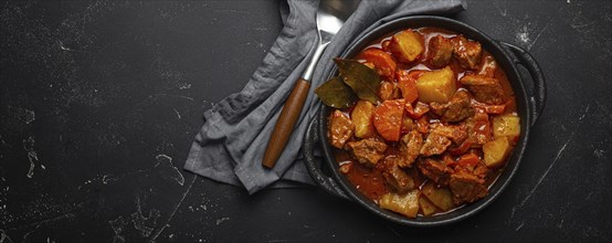 Beef meat stew with potatoes, carrot and delicious gravy in black casserole pot with bay leaves