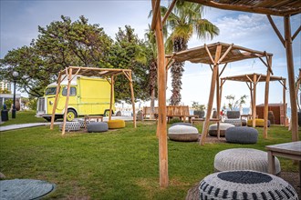 Yellow motorhome on a green meadow with rattan furniture and a view of the sea on a sunny day,