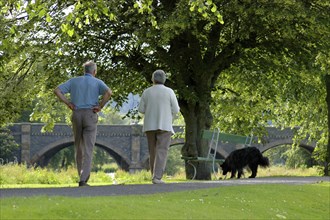 An elderly couple walking their dog in a park