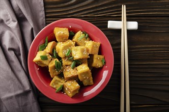 Flat lay view at crispy deep stir fried tofu cubes with chives in clay dish on wooden kitchen table