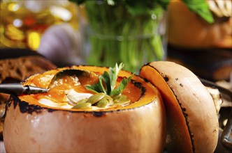 Homemade rustic pumpkin soup with seeds in pumpkin shell on kitchen table with bread aside