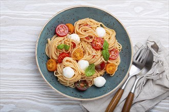 Delicious spaghetti with mozzarella, colourful cherry tomatoes, fresh basil on ceramic plate on