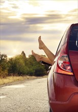 Female bare feet stick out of car window on mountain background. Travel concept