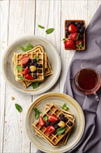 Flat view at belgian waffles served with strawberries and blackberries on white wooden kitchen