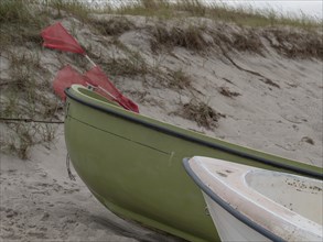 A green and white boat lying on the dune beach with red flags, ahrenshoop, zingst, baltic sea,