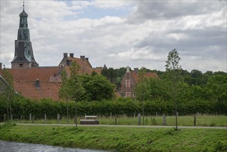 Quiet village scene with church tower, red roofs, green trees and a watercourse under a partly