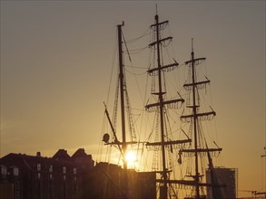 Silhouette of a sailing ship at sunset in front of a clear sky and some houses, Bremen, Germany,