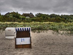 A beach chair with the number 21 stands on a sandy beach with dunes and clouds, ahrenshoop, zingst,