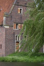 Detailed view of a medieval building with a red tiled roof and green trees in the background,