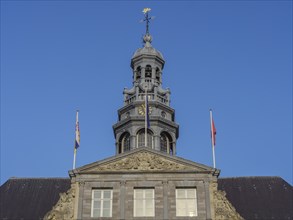 Close-up of a tower with complex architecture and two flags against a blue sky, maastricht.