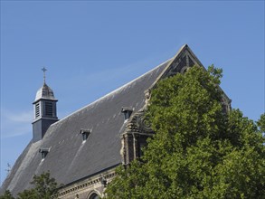 Historic church building, partly covered by trees under a blue sky, maastricht. netherlands