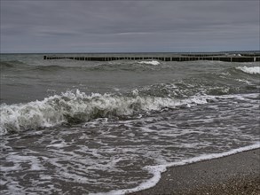 The ocean shows dramatic waves crashing against the beach. Dark, cloudy skies and wooden