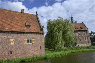 Historic brick building by the river with large trees in the background and cloudy sky, Raesfeld,