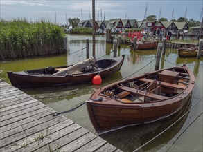 Harbour view with wooden boats, jetty and reeds, red flags and cloudy sky, ahrenshoop, zingst,