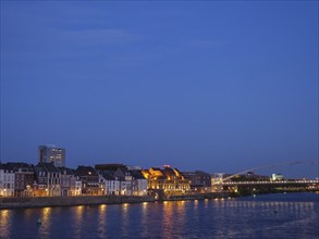 Riverbank with illuminated houses and a bridge during the blue hour, maastricht, the netherlands