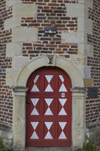 Historic red wooden door with white triangular patterns in a stone wall with bricks, Raesfeld,