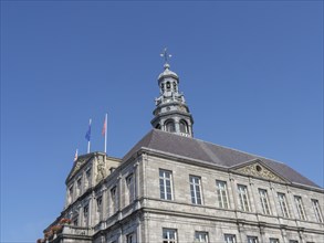 Historic tower building with waving flags and clear sky, maastricht. netherlands