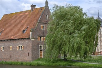 Small half-timbered building with red tiled roof by a moat, surrounded by green trees, Raesfeld,