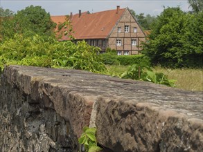 Brick country house with green trees and a stone wall in the foreground, Steinfurt, North