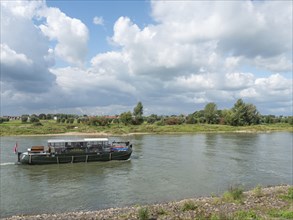 Boat sailing along a river under a partly cloudy sky with natural landscape, zutphen, netherlands