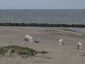 An empty beach with a few beach chairs, a calm sea and stone breakwaters in the background. A quiet