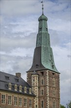 Historic onion dome with green copper roof on a building with brick walls under a cloudy sky,