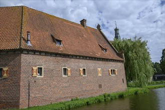 Historic brick building on the waterfront with roof tiles under open shutters under a cloudy sky,