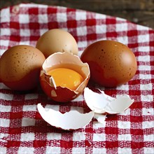 Cracked egg partially spilled on a checkered tablecloth, AI generated