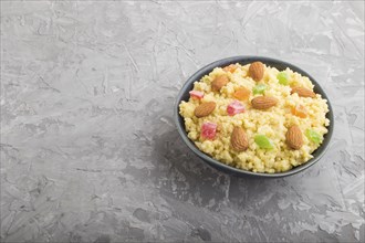 Millet porridge with candied fruits and almonds in blue ceramic bowl on a gray concrete background.