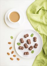 Chocolate candies with almonds and a cup of coffee on a white wooden background and green textile.