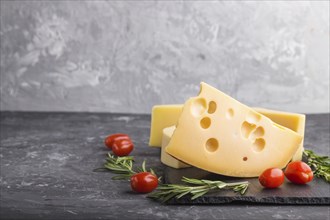 Various types of cheese with rosemary and tomatoes on black slate board on a black concrete