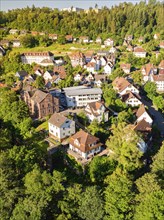 Aerial view of a town with many houses on a green hill surrounded by lush vegetation on a sunny