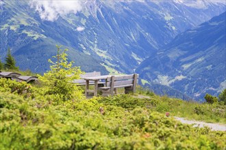 A bench on a hill with a view of the impressive mountain landscape under a partly cloudy sky,