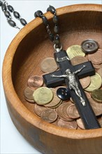 Crucifix with coins and buttons in a wooden bowl, church and money