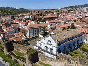 White historic building next to a wall, surrounded by red tiled roofs and trees, aerial view, city