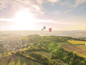 Several hot air balloons over a landscape with farmland and forest at sunset, Calw, Black Forest,