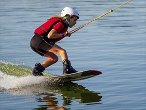 Boy or girl with wakeboard in the lake, red waistcoat, water sports, water skiing in the wake park