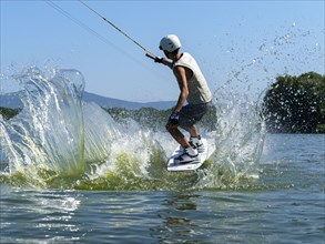 Young man jumping with wakeboard into the lake, water sports, water skiing in wakepark, Stráž pod