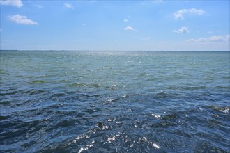 A calm summer's day on the Mediterranean with blue skies and soft clouds, through which the sun's