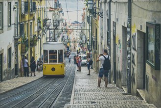 A yellow tram descends a steep, narrow alley full of charm in an urban setting, people taking