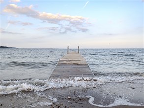 Wooden jetty leads into the sea at sunset, with calm waves and a pastel-coloured sky