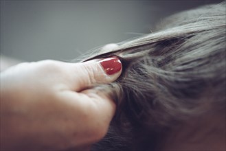 A hand with red nail varnish carefully holds a person's hair together