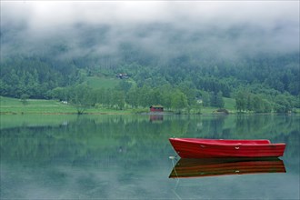 A small, red boat on a calm lake, idyll, surrounded by fog and green nature, Stryn, Mindesundet,