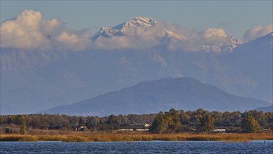 Snow-capped mountain peaks rise behind a landscape with water, Strofilia biotope, wetlands,