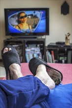 Couch potato, lazy man in comfy chair wearing worn slippers with big toes sticking through and