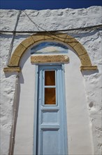 A building with a stone arch above a blue door shining in the sunlight, Chora, Old Town, Patmos,