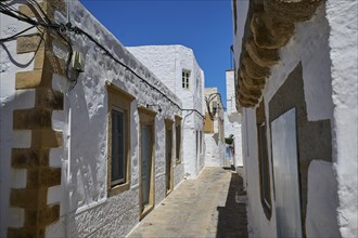 Narrow alley between white, historic buildings under a clear blue sky, Chora, main town Patmos,